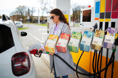 Symbolbild höhere Abgaben mit CO2-Gesetz durch Frau an der Tankstelle mit eingeblendeten Banknoten
