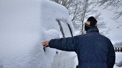 Verschneites Auto und eine Person, die daneben steht.