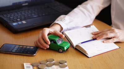 Person am Tisch mit Geld, Handy und Notizbuch.